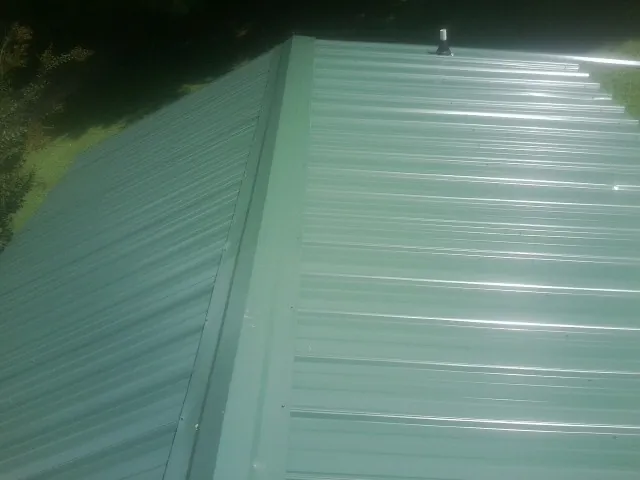New green metal panels meeting at the ridge of a roof — Flat Roof Repair work by our crew in Sandy