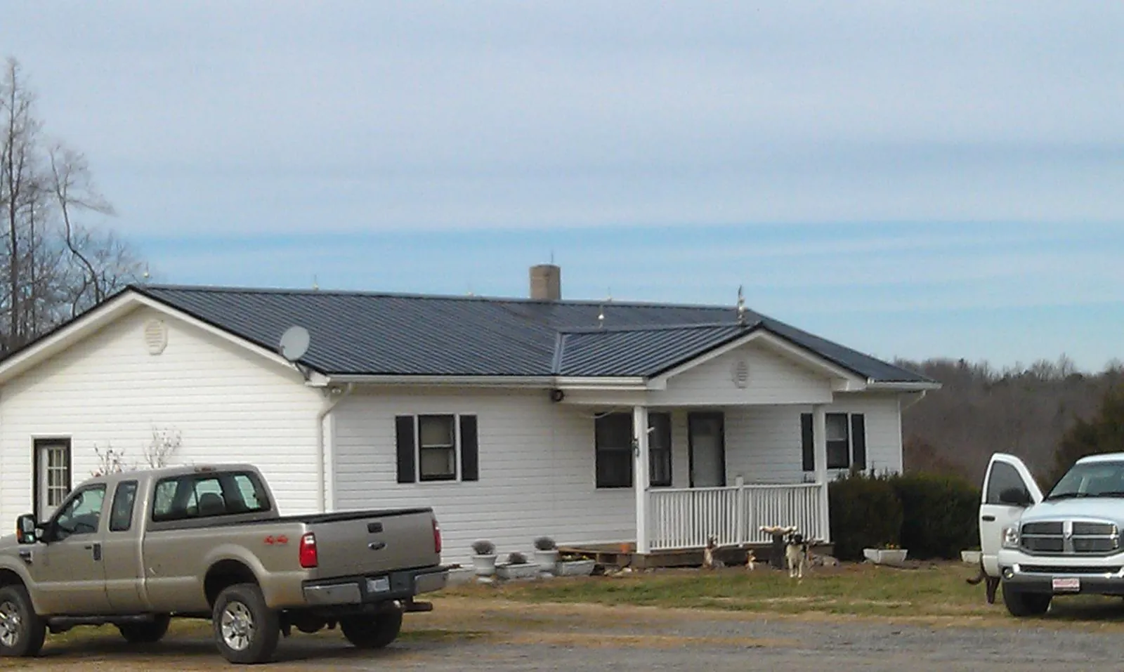 Finished dark metal roof on a white ranch home with work trucks parked in Sandy