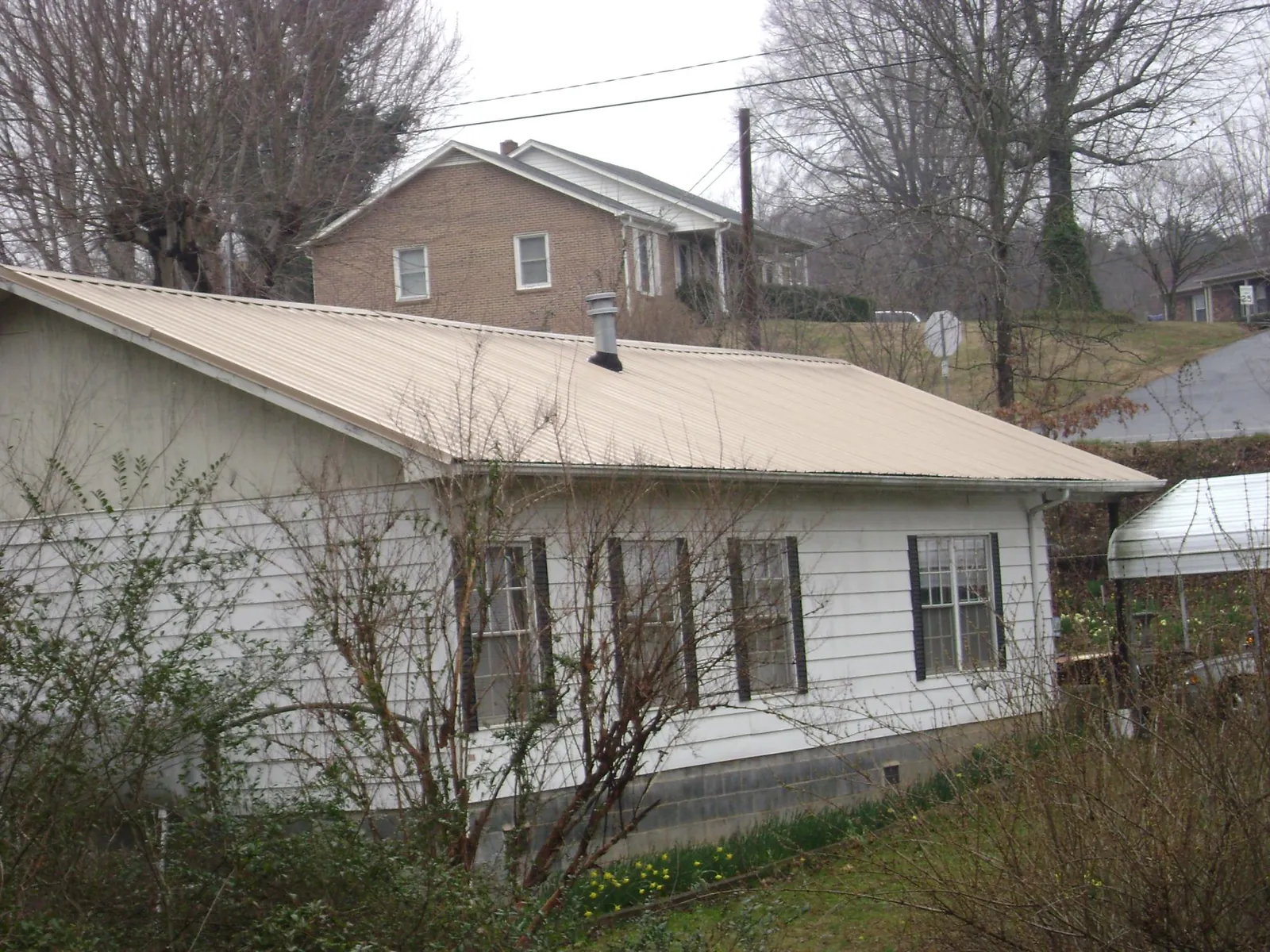 Tan metal roof on a white sided house set into a hillside — Commercial Roofing by Roofing Brothers in Sandy